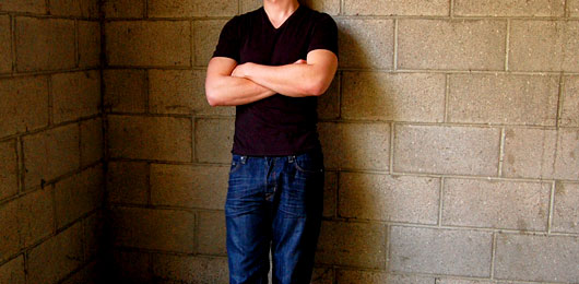 A man standing in front of a brick wall wearing a vneck