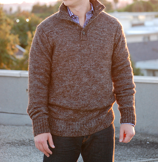 A man standing in front of a building in a sweater