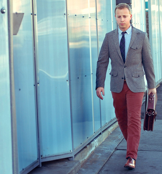 A man wearing a blazer and red pants and tie standing in front of a building