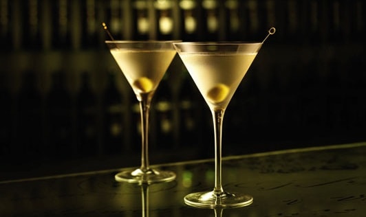 Two gin martinis side by side on a bar