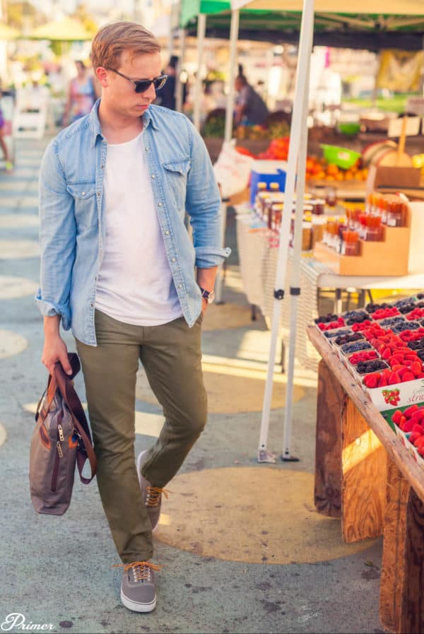 a man at a market wearing a chambray shirt over a shirt with fitted chino pants and slip on shoes