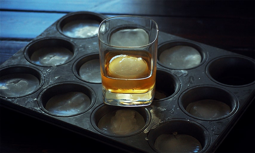 a cocktail glass on top of a muffin tray with ice cubes in the muffin cups