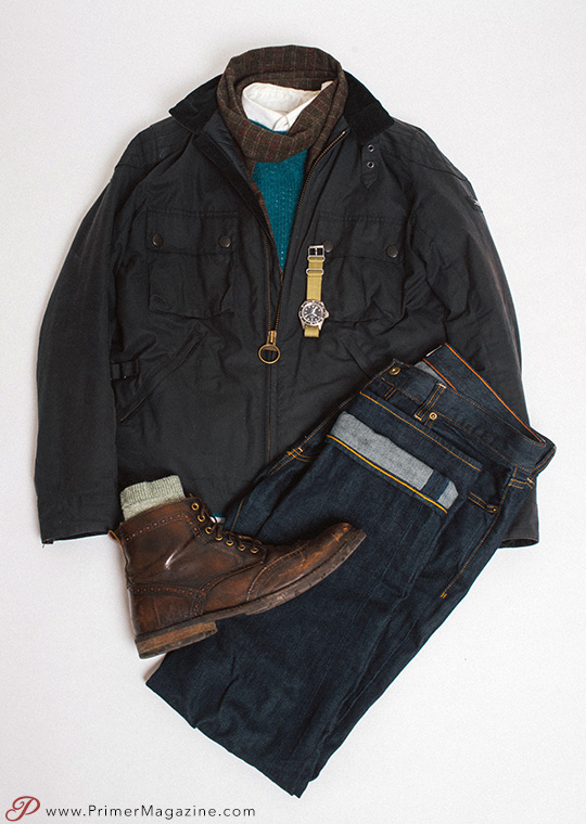 flatlay of waxed cotton jacket outfit including sweater, oxford shirt, dark denim, and wingtip boots