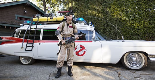 man wearing a ghostbusters uniform standing next to ghostbusters ecotmobile
