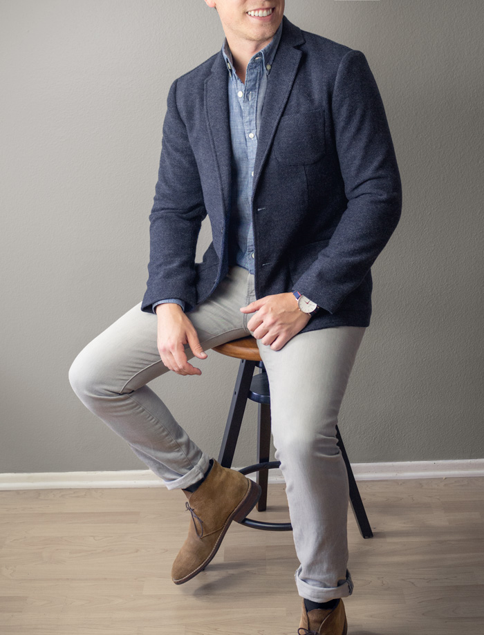 a man wearing a navy blazer over a chambray shirt with slim fit pants and boots