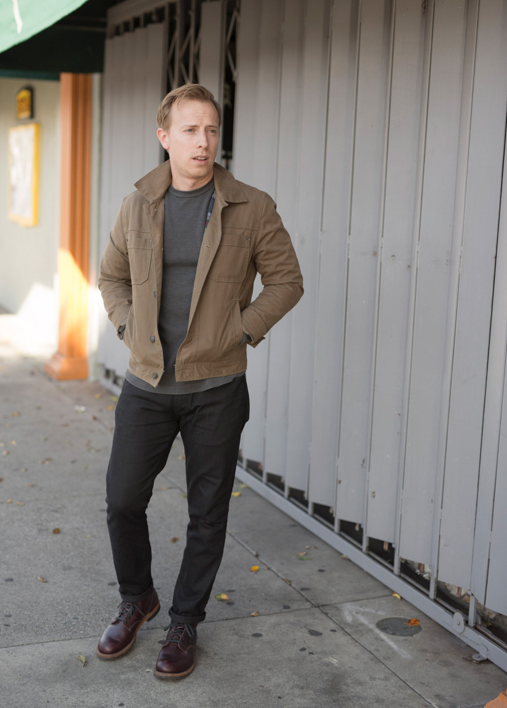 a man wearing a waxed canvas jacket over a shirt, pants, and boots