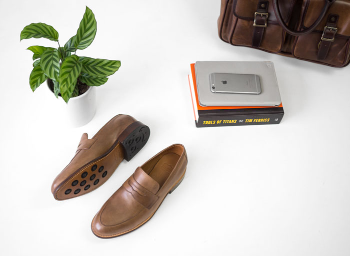 men tan loafers books phone briefcase flatlay white background