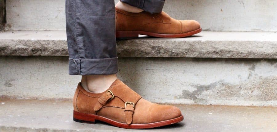 A pair of feet standing on a sidewalk wearing monk strap shoes