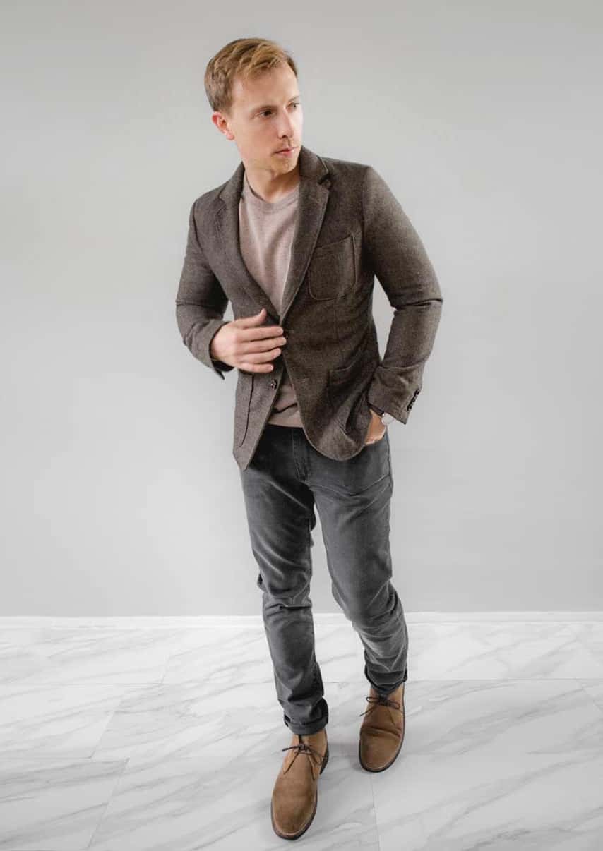 a man wearing a smart casual outfit of a sweater, blazer, jeans, and suede boots