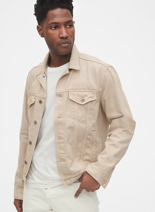 A person standing posing for the camera weraing a cream colored trucker jacket