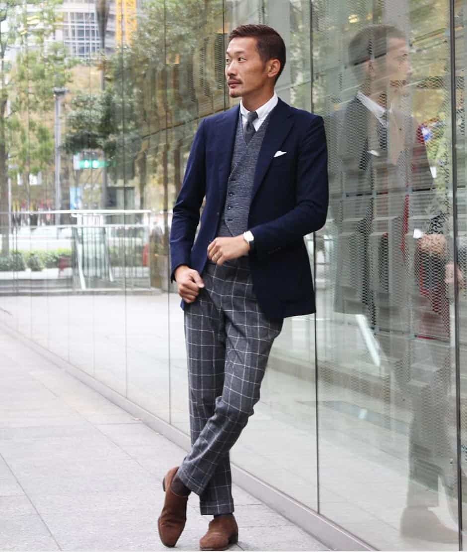 a man wearing a navy blazer over a shirt and vest with patterned trousers and dress shoes