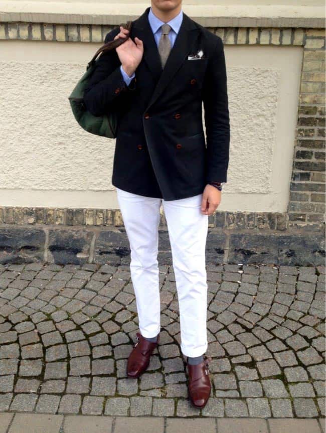 a man wearing a double breasted navy blazer over a shirt and tie and white pants with dress shoes