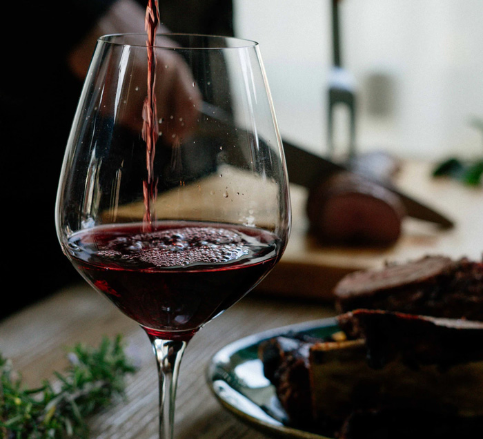 red wine poured into a glass with a carving of meat in the background
