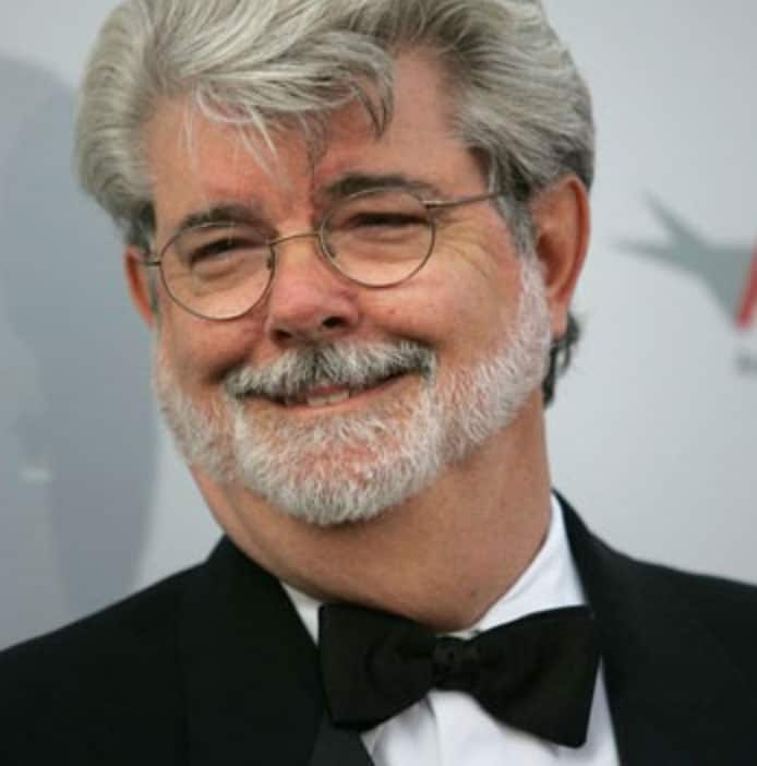 George Lucas wearing a suit and tie smiling at the camera