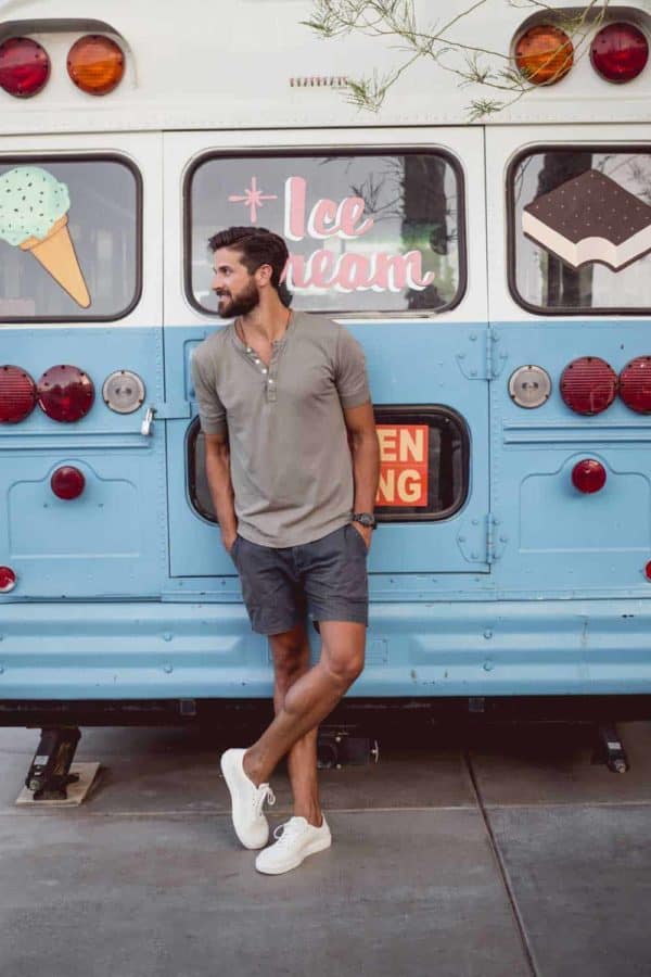 a man wearing a henley shirt, shorts, and white sneaker alternative to boat shoes