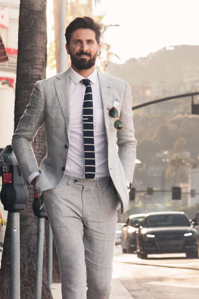 a man wearing a grey linen suit, white shirt, and striped knit tie