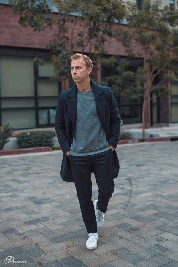 men's smart casual outfit example with topcoat, gray sweatshirt, black pants, and white sneakers