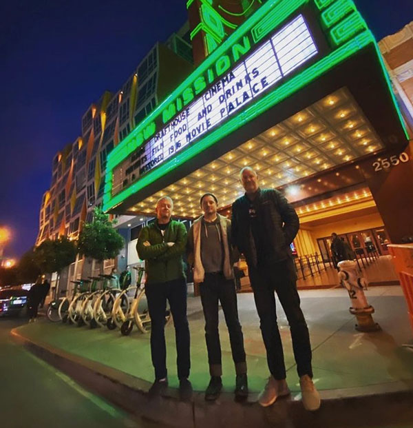 three men standing in front of a movie theatre 