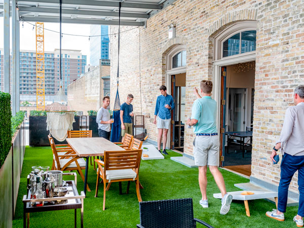 A group of people playing cornhole in front of a building