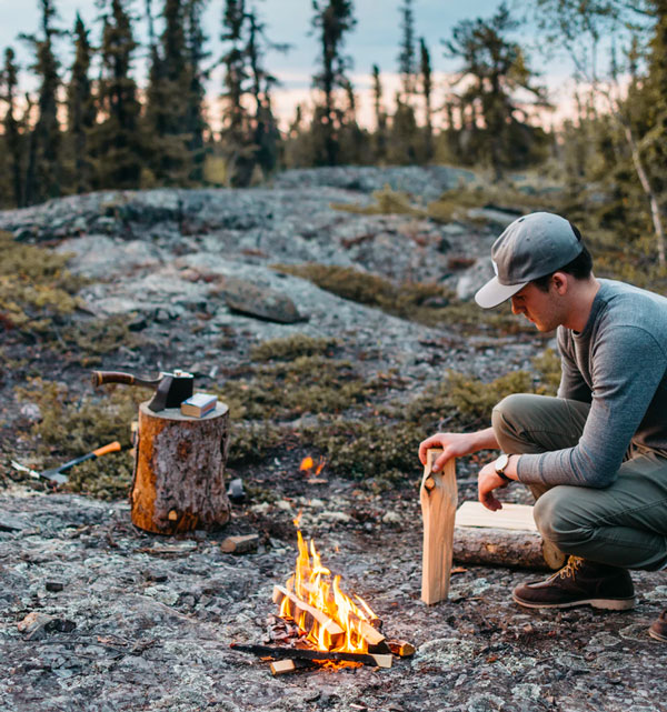 a man outdoors building a fire with firewood