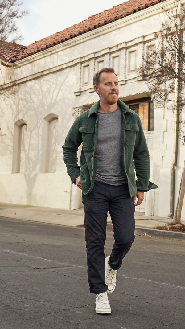 a man wearing a fleece shirt jacket, shirt, pants, and lace up sneakers