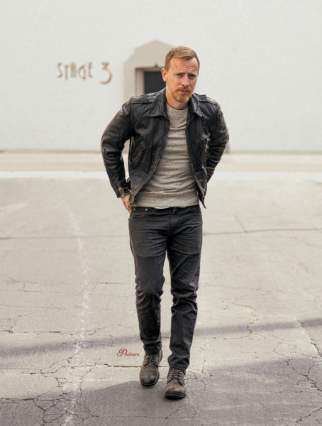 a man wearing a black leather jacket layered over a sweatshirt, jeans, and boots