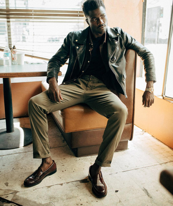 a man wearing a leather jacket over a shirt, pants, and loafers from Buck Mason 