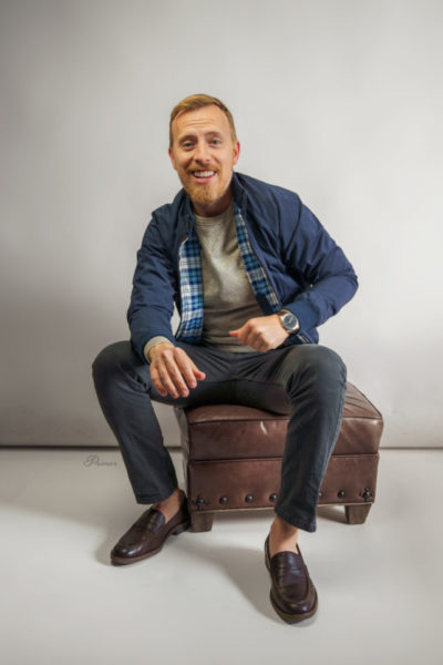 man wearing a dark blue harrington jacket dark jeans and dark brown penny loafer shoes