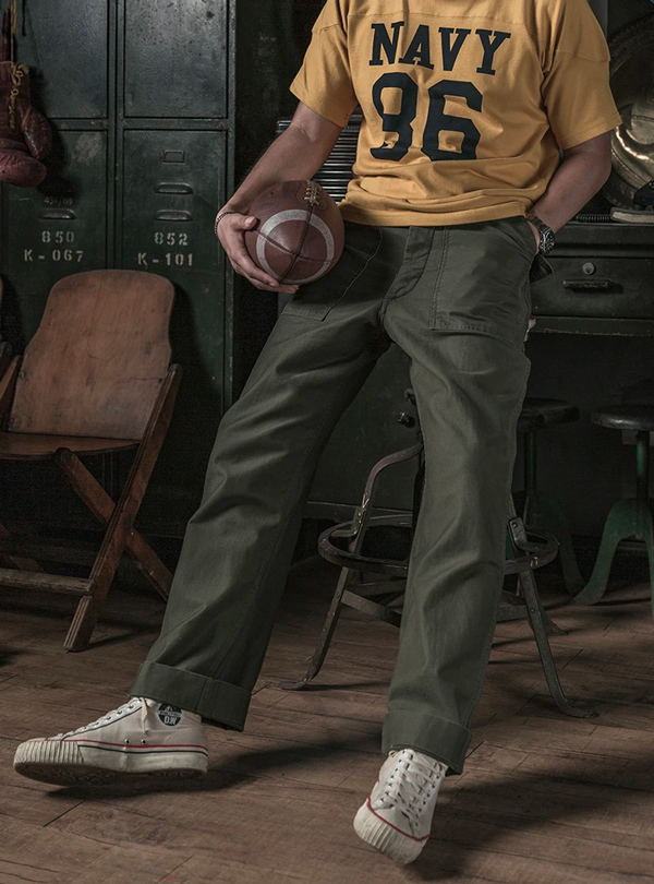 a man wearing a jersey shirt with fatigue pants and carrying a football