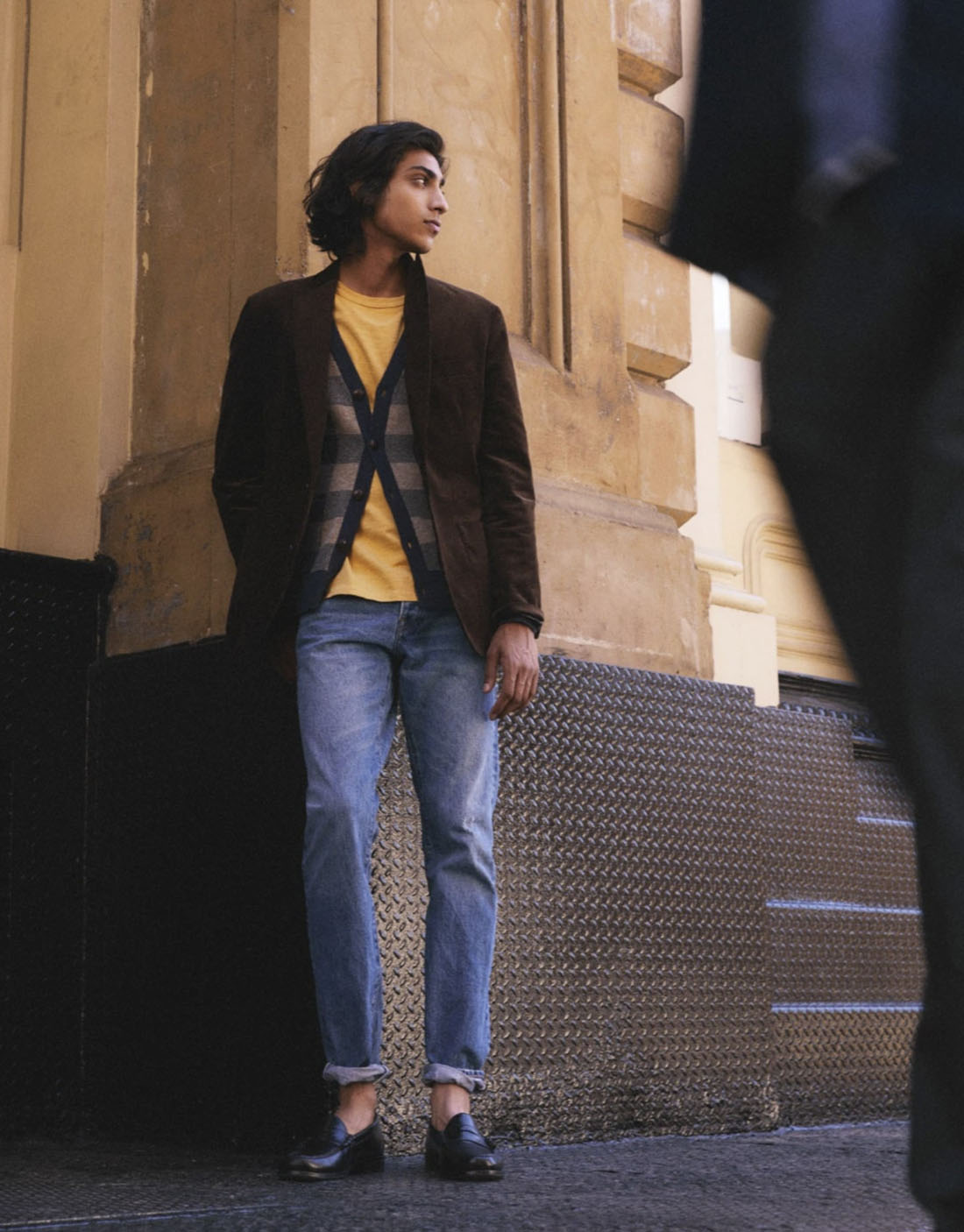 man wearing a brown jacket yellow shirt and blue jeans