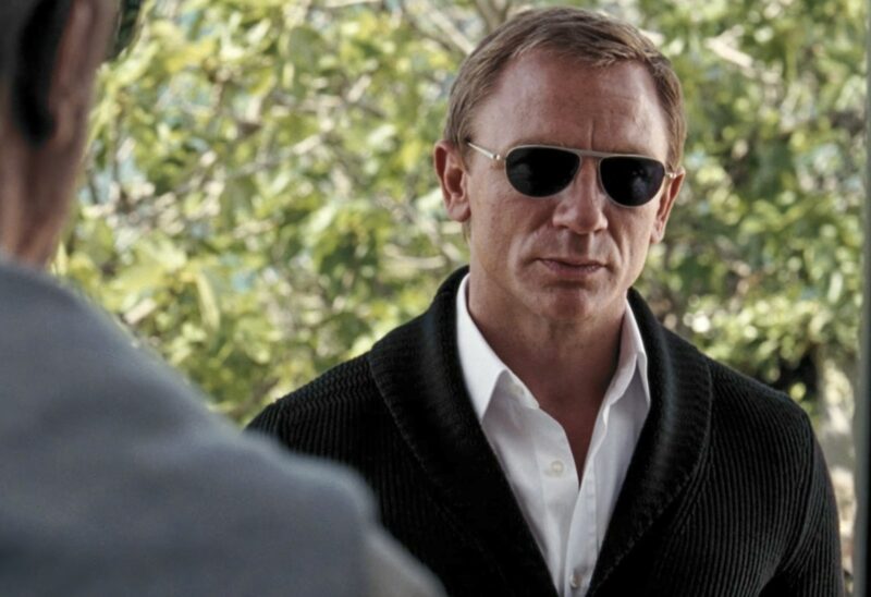 daniel craig james bond wearing dark sunglasses and a shawl collar cardigan over an oxford shirt
