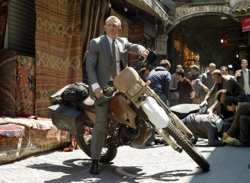 daniel craig james bond on a motorcycle wearing a grey suit