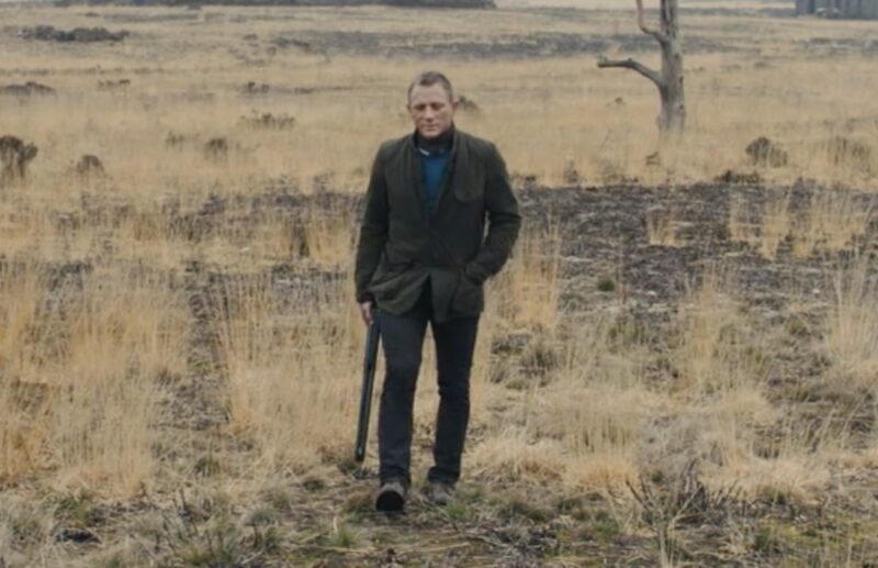 daniel craig james bond wearing a sport jacket over a sweater and pants and walking in a field