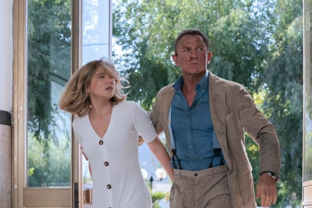 daniel craig in james bond wearing a tan suit and collared shirt in an entranceway with a woman