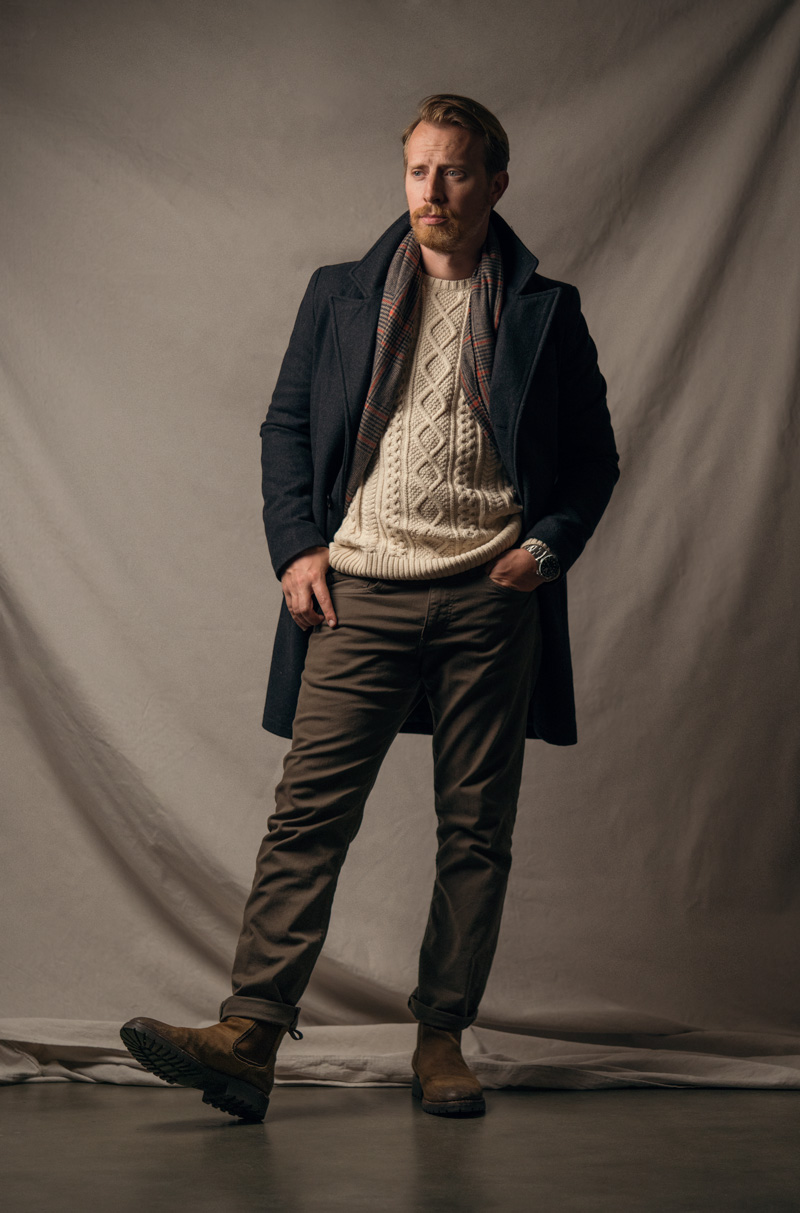 a man wearing an overcoat with a nautical sweater, jeans, and chelsea boots