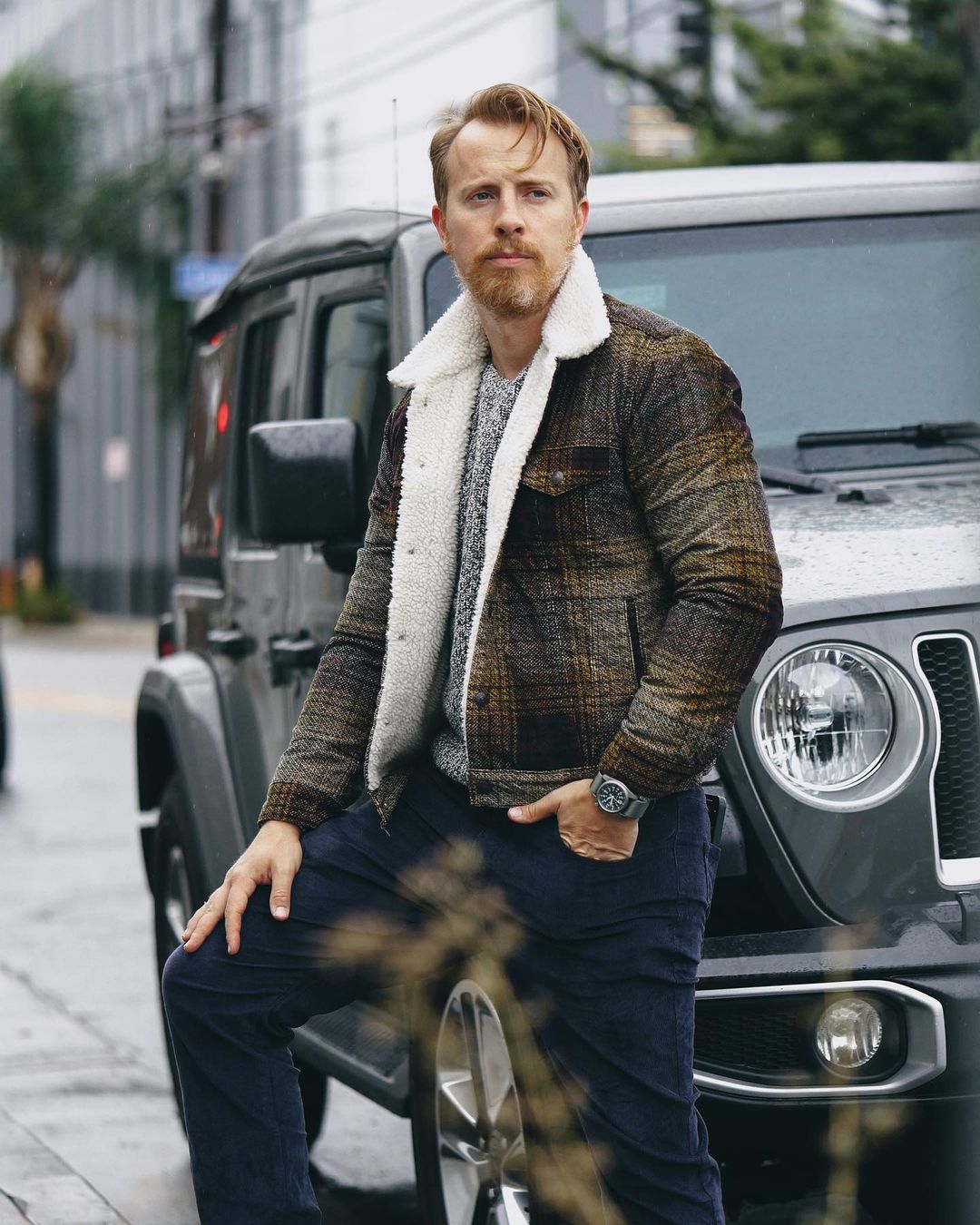 a man wearing a plaid pattern shearling jacket over a sweater and jeans