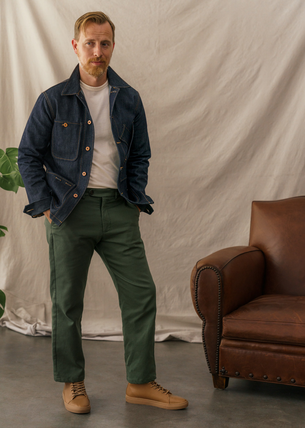 man wearing denim chore coat with relaxed fit olive pants and tan sneakers