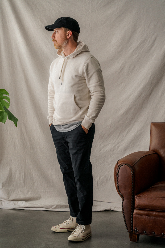 man in monochrome minimalist white and black outfit with white hoodie, black pants, black cap, and canvas sneakers