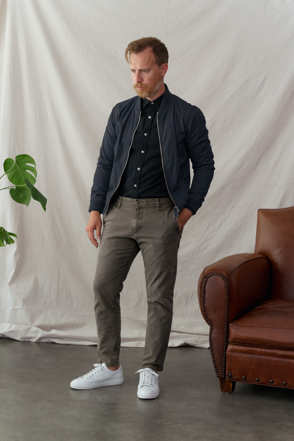 men's smart casual outfit with bomber jacket, black button up shirt, tan chino pants, andand white sneakers