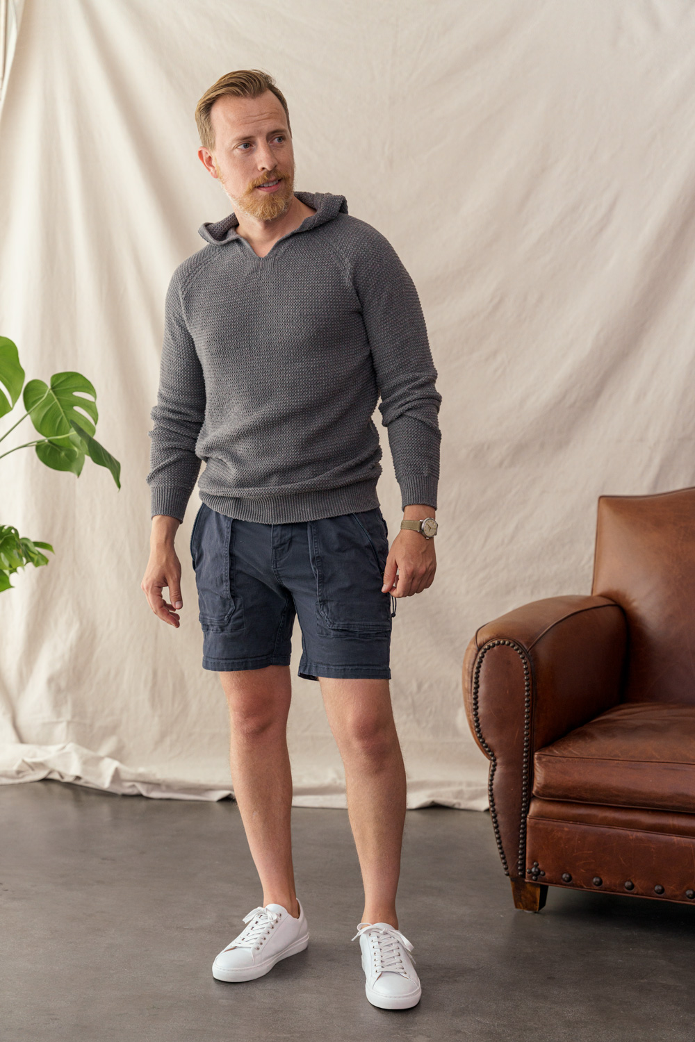 men's summer outfit with knit sweater hoodie, navy shorts, and white sneakers