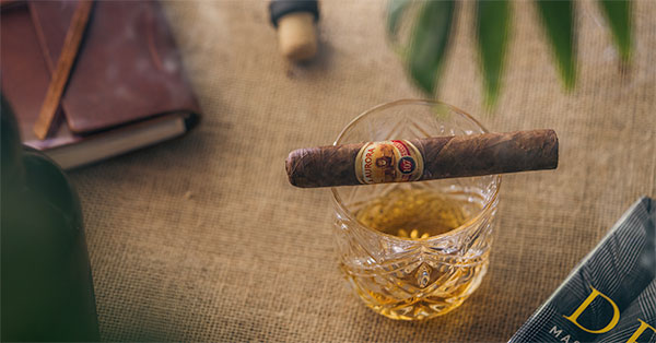 a cigar balanced on the rim of a whiskey glass