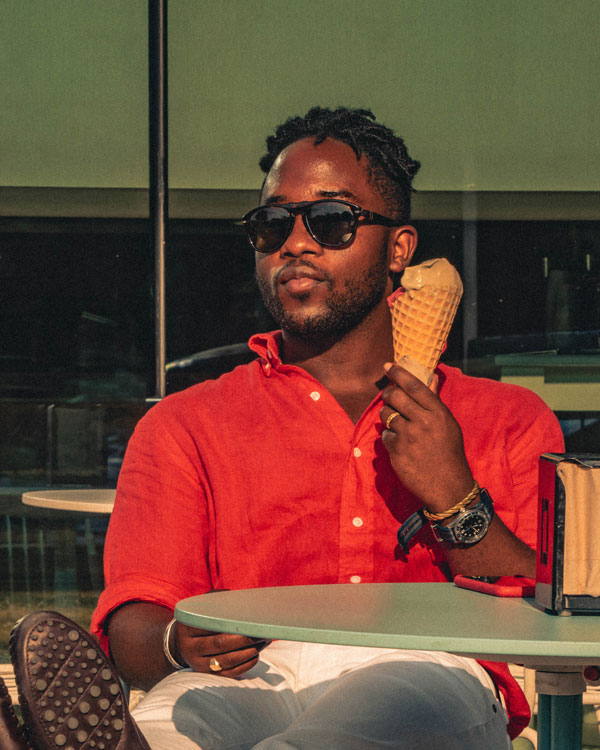 Daniel Baraka in a red linen shirt eats an ice cream cone