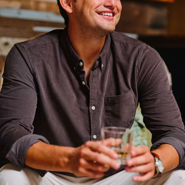 a man wearing a button up corduroy shirt and holding a cocktail glass