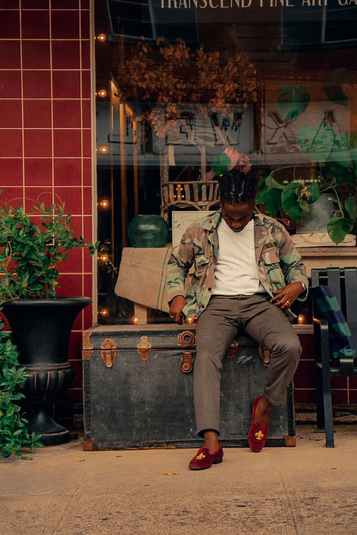 man wearing a camo jacket with white t-shirt, dress pants, and velvet slippers