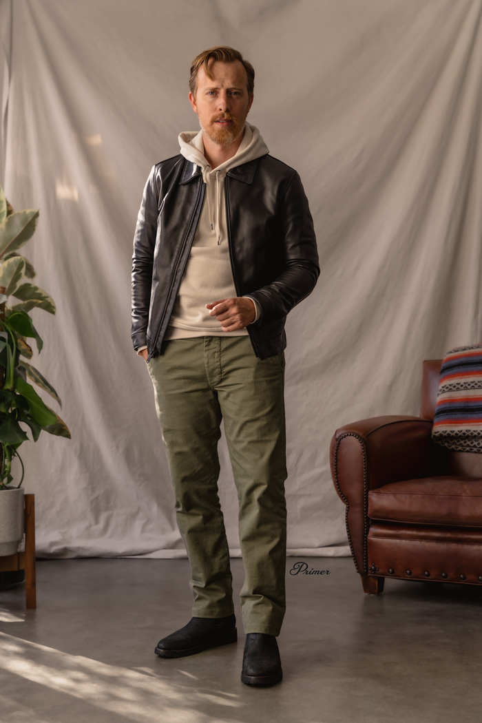 men's leather jacket and boots outfit with black leather jacket, cream hoodie sweatshirt, olive chinos, and matte black chelsea boots