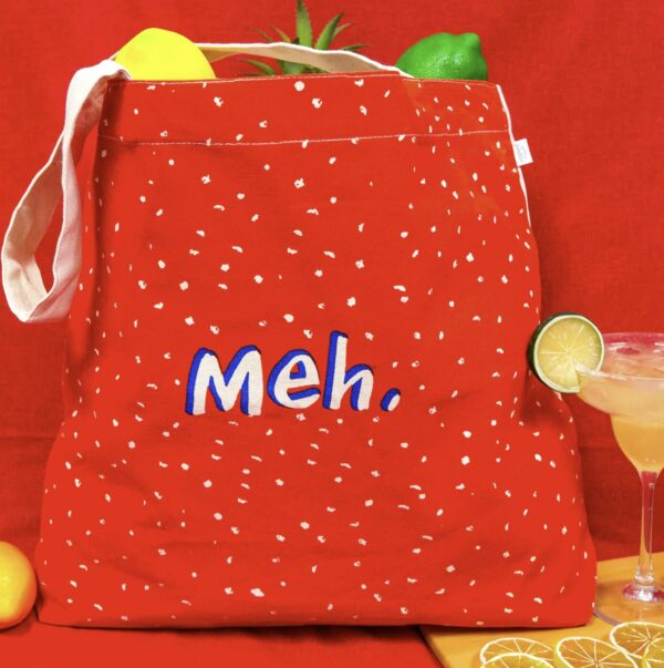 a red tote bag with meh wording on the center of the bag