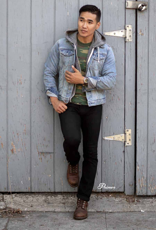 a man wearing black jeans, brown boots, a blue trucker jacket and a gray hoodie