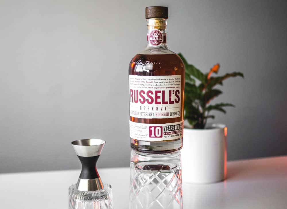 a bottle of russell reserve bourbon whiskey and a cocktail jigger on cocktail glasses