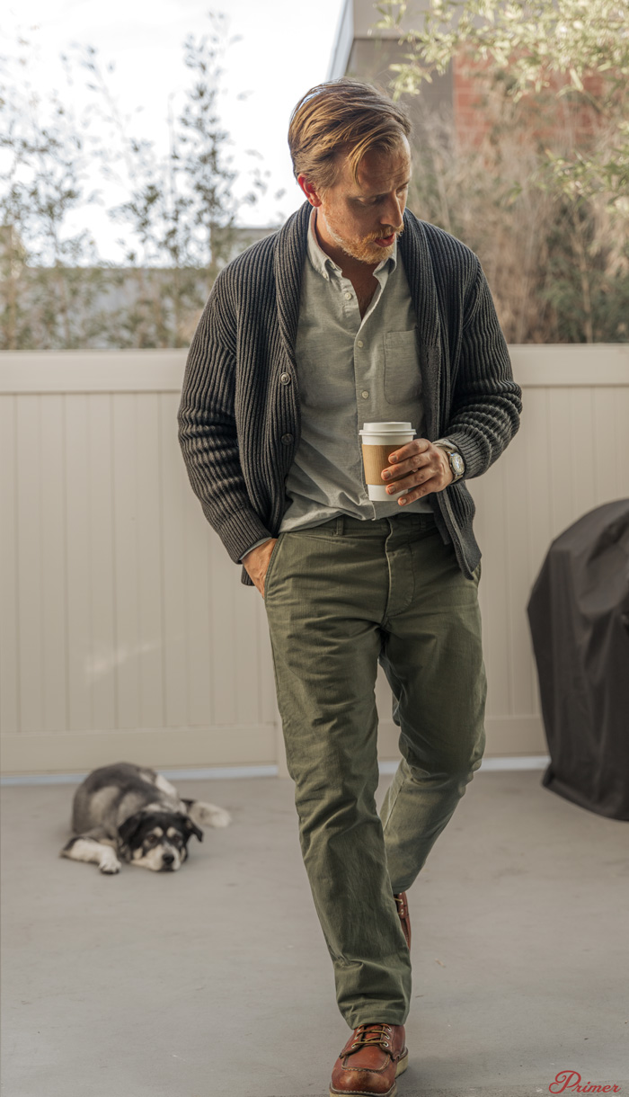 buck mason officer chino review - man wearing pants with shawl collar sweater in front of a dog