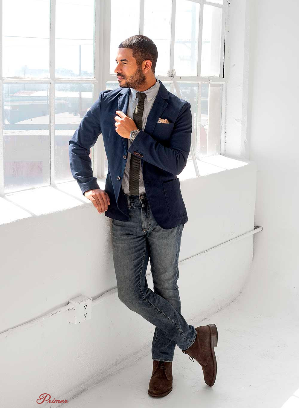 a man wearing a navy sportcoat over a shirt and tie, white jeans and boots